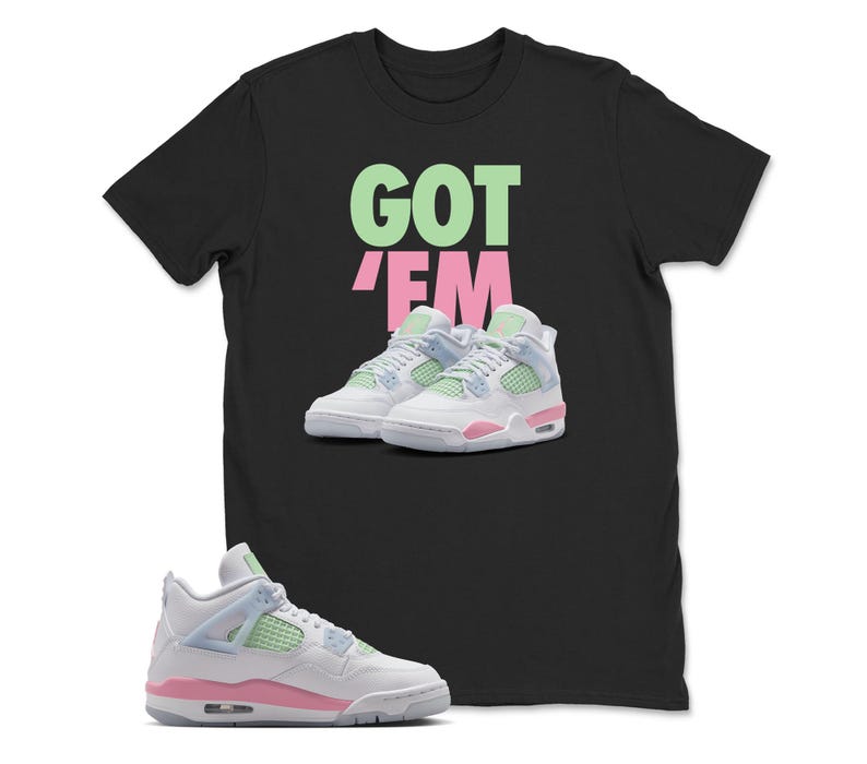 May include: Black t-shirt with the words "GOT 'EM" in green and pink. The shirt features a graphic of white, pink, and light blue trainers. A pair of matching trainers is in the foreground.