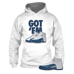 May include: White hoodie with a front pocket and a drawstring hood. The hoodie features the text "GOT 'EM" in navy blue, along with an image of white and navy blue sneakers. A single sneaker is shown at the bottom.