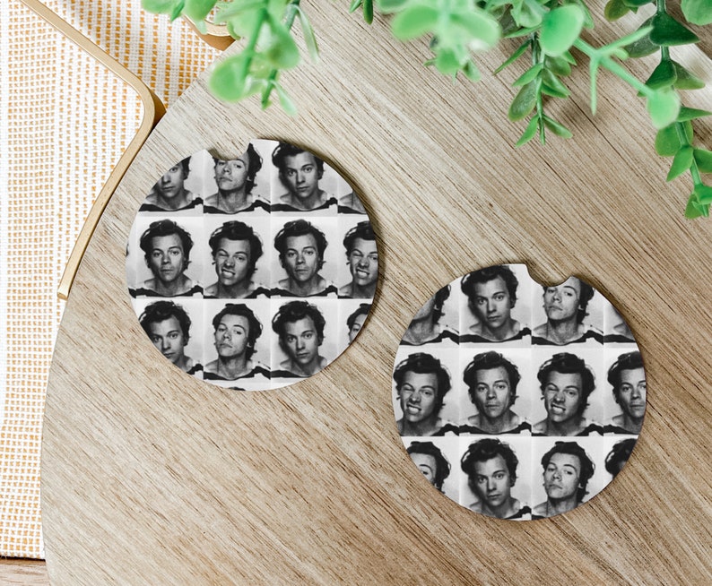 May include: Two round, white coasters featuring a black and white photograph of a man's face repeated in a grid pattern. The coasters are on a wooden surface.