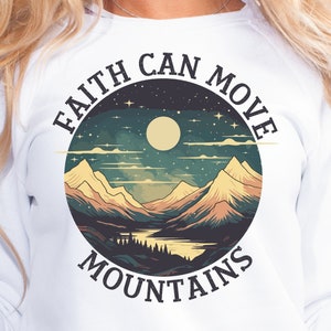 Op de afbeelding: Witte longsleeve sweatshirt met een grafische print van een berglandschap met een volle maan en sterren. De tekst "FAITH CAN MOVE MOUNTAINS" is rond de afbeelding gedrukt.