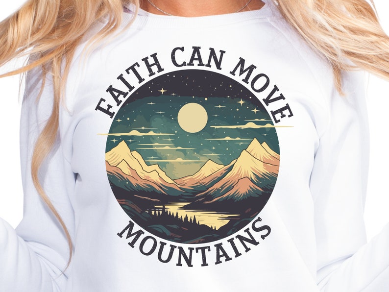 Op de afbeelding: Witte longsleeve sweatshirt met een grafische print van een berglandschap met een volle maan en sterren. De tekst "FAITH CAN MOVE MOUNTAINS" is rond de afbeelding gedrukt.