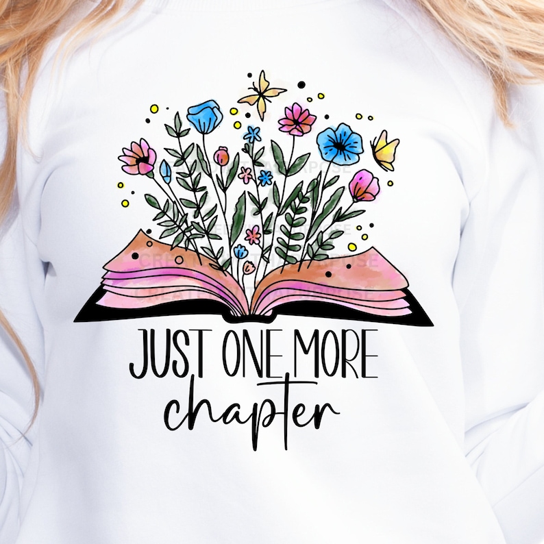 May include: White sweatshirt featuring a watercolor illustration of an open book with colorful flowers and butterflies emerging from the pages. The text "JUST ONE MORE CHAPTER" is printed below the book in black.