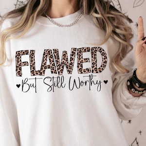 Op de afbeelding: Wit sweatshirt met een luipaardprint die "Flawed But Still Worthy" in zwarte tekst zegt.
