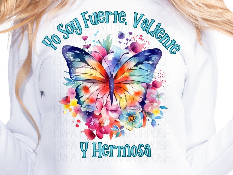 May include: A white t-shirt with a watercolor design of a butterfly surrounded by flowers. The text "Yo Soy Fuerte, Valiente y Hermosa" is written in blue around the butterfly.