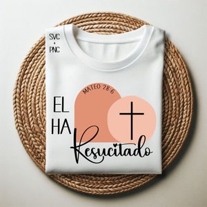 May include: White t-shirt with a black graphic design that says "EL HA Resucitado" with a cross and a peach colored heart shape. The text "MATEO 28:6" is also included in the design.