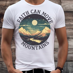 Op de afbeelding: Wit T-shirt met een cirkelvormig grafisch ontwerp met een bergketen, een meer, een volle maan en sterren. De tekst "Faith Can Move Mountains" staat rondom de afbeelding.