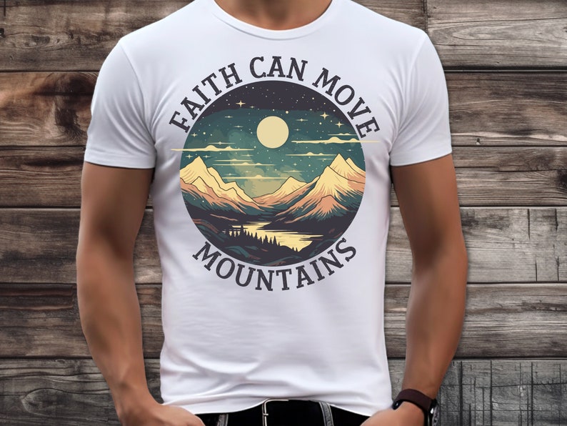 Op de afbeelding: Wit T-shirt met een cirkelvormig grafisch ontwerp met een bergketen, een meer, een volle maan en sterren. De tekst "Faith Can Move Mountains" staat rondom de afbeelding.