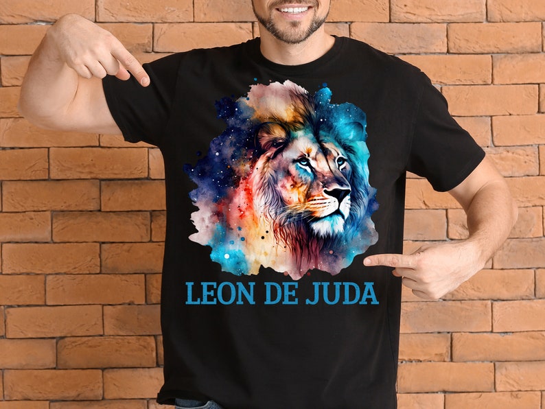 May include: A black t-shirt with a colorful watercolor illustration of a lion's head. The lion's mane is a mix of blue, orange, and yellow. The background is a galaxy-like pattern with stars. The text "LEON DE JUDA" is printed in blue below the lion's head.