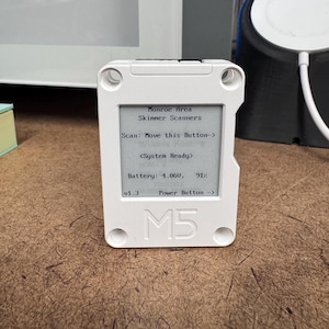 May include: A white M5 device with a screen displaying text: "Monroe Area Skinner Scanners", "Scan: Move this Button->", "<System Ready>", "Battery: 4.060V, 91%", and "Power Button ->". The device has a rectangular shape with rounded corners and four screw holes.