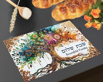 May include: A rectangular placemat featuring a colorful tree illustration with intricate branches and leaves in shades of blue, green, orange, and gold. The text "שבת שלום" and "Rosenfeld Family" is printed in black on the right side.