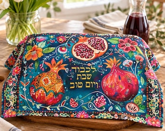 May include: A rectangular fabric cover featuring a dark teal background with colorful illustrations of pomegranates, flowers, and leaves. The Hebrew text "לכבוד שבת ויום טוב" is printed in gold in the center. The fabric has a decorative border.