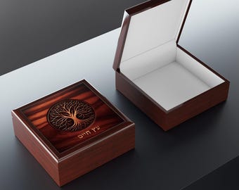 May include: A square wooden keepsake box with a dark mahogany finish. The lid features a circular gold tree of life graphic and Hebrew text that reads עץ חיים. A second identical box is shown open, revealing a plain white interior lining.