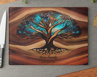 May include: A rectangular cutting board with a wood grain pattern featuring a central tree illustration with brown branches and vibrant blue foliage. The text "Stein Family" and "03-23-24" is printed in black below the tree roots.