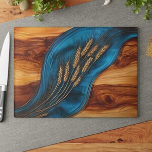 May include: A rectangular wooden cutting board featuring a central, flowing wave of translucent blue resin. The surface is decorated with a detailed, golden-brown wheat stalk design embedded within the resin, contrasting against the natural wood grain.