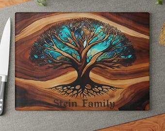 May include: A rectangular wooden cutting board featuring a dark brown wood grain pattern and a central illustration of a tree with intricate branches and vibrant turquoise blue leaves. The text "Stein Family" is printed in dark brown below the tree.