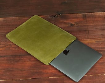 Könnte beinhalten: Eine rechteckige olivgrüne Laptoptasche mit glatter Oberfläche, die teilweise einen dunkelgrauen Laptop mit einem sichtbaren schwarzen Apfel-Logo auf dem Deckel enthält. Die Tasche ist mit einer offenen Seite zum Einschieben des Geräts gefertigt.