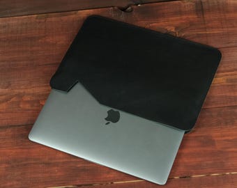 May include: A dark gray laptop with a metallic finish and a centered apple logo partially inserted into a black sleeve. The sleeve features a diagonal cutout design on the top edge, revealing the laptop surface and its iconic brand emblem clearly.