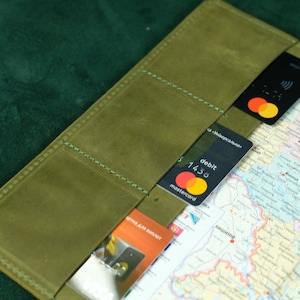 May include: An olive green leather passport or document holder featuring multiple interior card slots. The slots contain two black Mastercard debit cards and one orange Visa card. A detailed map of Ukraine is visible tucked into the holder.