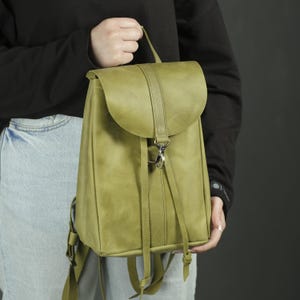 Pu&ograve; includere: Uno zaino in pelle verde salvia caratterizzato da una patta ripiegabile con cinturino verticale e chiusura con moschettone in metallo argentato. La borsa presenta lunghi lacci in pelle sul davanti e spallacci regolabili.