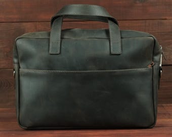 May include: A dark charcoal gray leather briefcase featuring a rectangular silhouette, two top handles, a zippered main compartment, and a horizontal front pocket with a visible zipper pull. The surface has a matte, smooth finish.