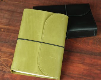 May include: A lime green leather journal with a curved flap closure and a thin black elastic band wrapped horizontally around the cover, positioned in front of a second black leather journal of the same design.