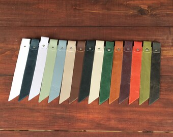 May include: A collection of fifteen long, narrow leather strips arranged in a row, each featuring a single metallic rivet at the top. The strips are presented in a variety of colors including white, black, green, blue, tan, brown, and orange.