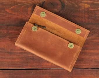 May include: A tan leather wallet featuring a fold-over flap design with three circular brass-toned snap fasteners. The wallet has a smooth exterior finish and a visible interior texture, with a small metal zipper pull visible near the top fold.