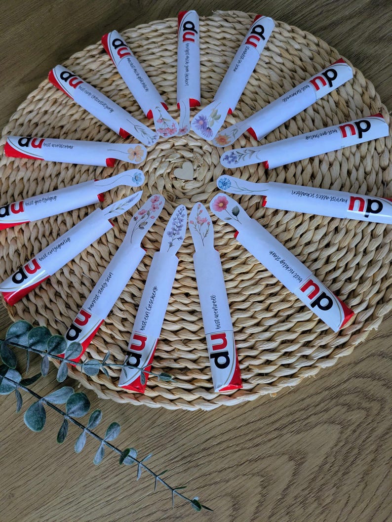 May include: A collection of white and red wrapped products arranged in a circular pattern on a woven mat. Each product features floral designs and text. The products are arranged around a small wooden heart.