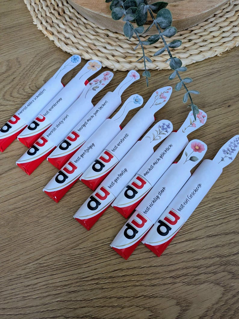May include: A collection of white and red candy bars with floral designs and German text. Each bar has a different message, such as "You are wonderful" and "You make me happy."