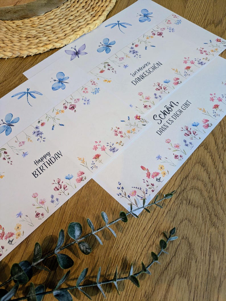 May include: White greeting cards with watercolor floral and insect designs. The cards feature dragonflies, butterflies, and floral borders in pink, blue, and yellow. Text includes "Happy Birthday" and other phrases.