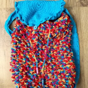 May include: A colourful, handmade crochet backpack. The bag has a bright blue top and straps, and a textured body in red, yellow, blue, and pink. It features a drawstring closure and a button detail.