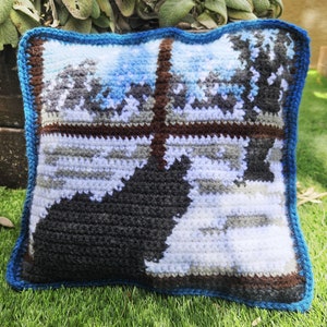 Könnte beinhalten: Ein gehäkeltes Kissen mit einem blauen Rand und einem Pixel-Design einer Winterszene. Das Design zeigt eine verschneite Landschaft mit Bäumen und einer dunklen Silhouette einer Figur.