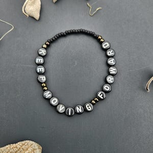 May include: Black beaded bracelet with white letters spelling "KEEP MOVING FORWARD".