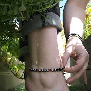 May include: Black beaded ankle bracelet with white lettering spelling "heart made full" with red beads between each word.