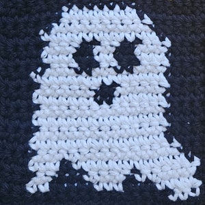 May include: A white crocheted ghost with black eyes and a mouth, against a black background.
