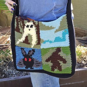May include: A black crocheted shoulder bag with a colorful patchwork design featuring a ghost, a snake, a bat, and a bear.
