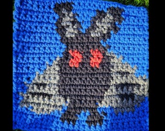 Könnte beinhalten: Gehäkeltes Quadrat mit einem schwarzen und grauen Fledermaus-Design mit roten Augen auf blauem Hintergrund.