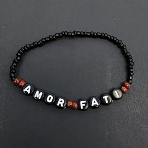 May include: Black beaded bracelet with white letter beads spelling out "AMOR FATI".
