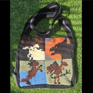 May include: A crocheted tote bag with a black strap and four squares featuring different colored dragons. The squares are black, orange, blue, and green.