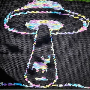 May include: A black crochet blanket with a white, pink, yellow, and blue crocheted mushroom design.