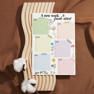 Könnte beinhalten: Ein Wochenplaner mit floralem Design und dem Text "A new week fresh start" und "You got this". Der Planer hat sechs Abschnitte für jeden Tag der Woche und einen Abschnitt für das Wochenende. Jeder Abschnitt hat einen Platz zum Schreiben und eine Checkliste.