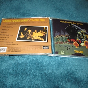 May include: A CD case with a brown background and a picture of a band on the front. The title of the CD is "Heads Hands & Feet - Tracks File".