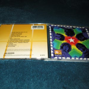 May include: A compact disc case with a colorful image of a band on the front. The back of the case lists the songs on the album: "Faster Than the Speed of Life", "Turned Up Your Radio", "None of Your Doing", "Spiritual Fantasy", "Don't Step on the Grass, Sam", "Magic Carpet Ride", "Disappointment Number Unknown", "Lost and Found by Trial and Error", "Moog Podge, Strained Through", "A Leslie", "Resurrection", "Reflections".