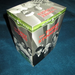 May include: A green and white box with the text "The Three Stooges Collector's Series 5 Pack" on the front. The box features a black and white photo of the Three Stooges.