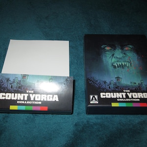 May include: A black and white box with the text "The Count Yorga Collection" on the front. The box has a colorful stripe across the bottom. The box is sitting on a blue surface.