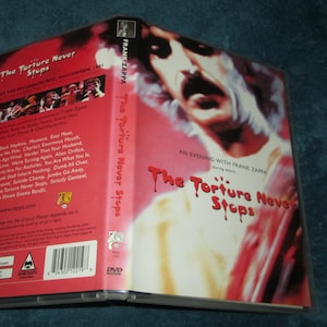 May include: DVD case with a red and white background. The front cover features a close-up of Frank Zappa's face. The title of the DVD is "The Torture Never Stops". The back cover lists the songs included on the DVD.