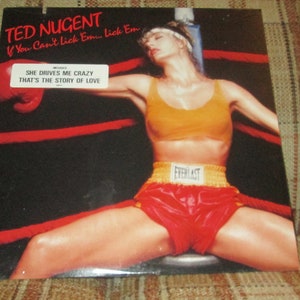 May include: A vintage vinyl record cover featuring a woman in a boxing ring wearing a yellow sports bra and red boxing shorts with the text "TED NUGENT If You Can't Lick Em... Lick Em SHE DRIVES ME CRAZY THAT'S THE STORY OF LOVE EVERLAST"