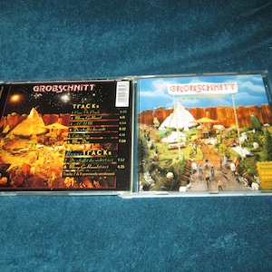 May include: A CD case with a black and white image of a miniature village on the front and a track list on the back. The CD case is titled "Grobschnitt -  Wings of Change".