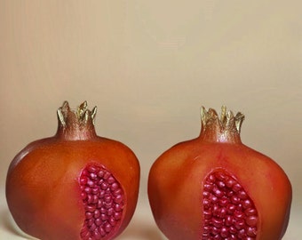 May include: Two red pomegranate-shaped candles with gold accents. The candles are detailed with a realistic depiction of the fruit's seeds.