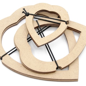 Peut inclure: Trois cadres en bois entrelacés en forme de cœur, reliés par des cordons élastiques noirs. Les cadres sont en bois brun clair et sont disposés sur un fond blanc. Le design suggère un projet artisanal ou de bricolage.
